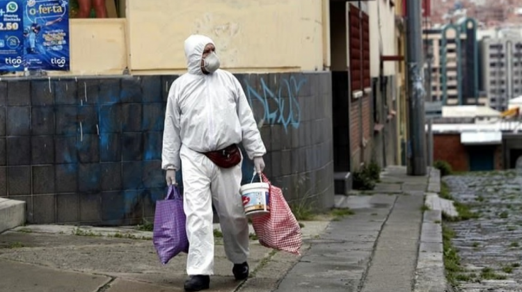 Un hombre con traje de bioseguridad camina con bolsas de alimentos en la ciudad de La Paz. Foto: Reforma