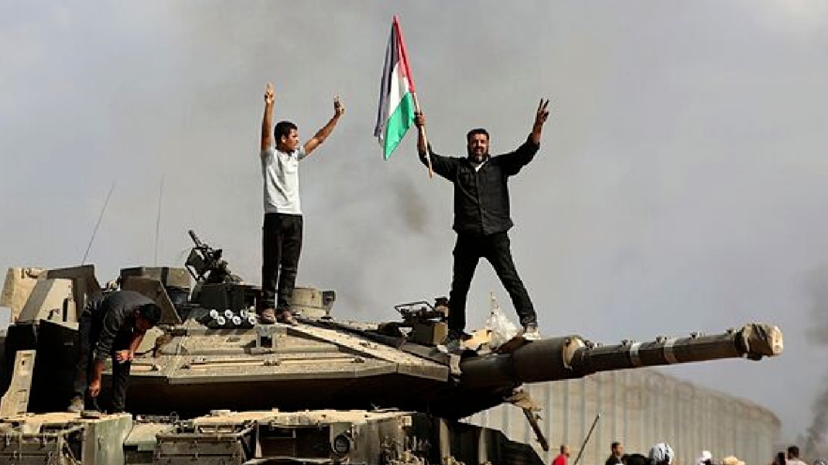 Dos personas levantan la bandera de palestina sobre un tanque.